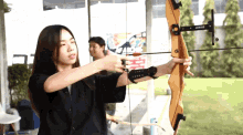 a woman is holding a bow and arrow with a sign in the background that says arrows