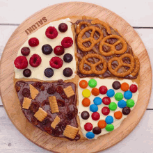 a wooden cutting board has four slices of pizza with different toppings including m & m 's and pretzels