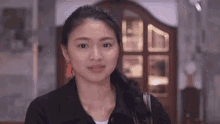 a woman in a black jacket is standing in front of a door and smiling .