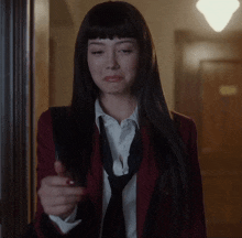 a woman wearing a red jacket and black tie is pointing at the camera