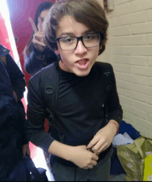 a young boy wearing glasses and a black shirt is standing in front of a brick wall