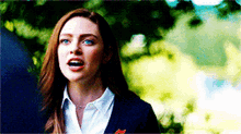 a woman in a suit and white shirt is standing in front of trees and trees .