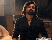 a man with long hair and a beard is wearing a black shirt with @mikelvelayudham on the bottom