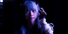 a woman with blue hair is standing in a dark room holding her hair .