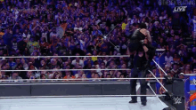 a man is carrying another man on his shoulders in a wrestling ring while a crowd watches .
