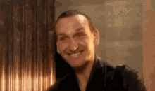 a man is smiling and looking at the camera while standing in front of a window .