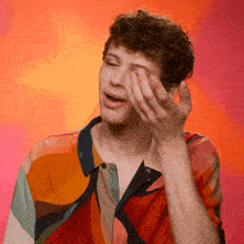 a man in a colorful shirt is covering his eyes with his hands