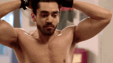 a shirtless man with his hands on his head looks at the camera
