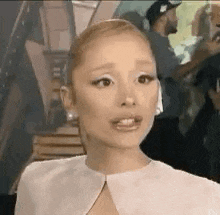 ariana grande is wearing a white shirt and earrings and making a surprised face .