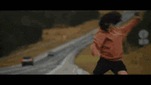 a woman is jumping in the air on a highway while a car is driving behind her .