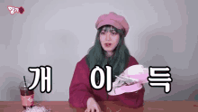 a woman with green hair and a pink hat is sitting at a table with a cup of coke .