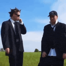 two men in suits and ties standing in a grassy field
