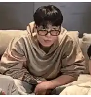 a man wearing glasses and a sweatshirt is sitting on a couch .