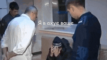 a man in a white shirt is talking to a man in a black hat while another man in a blue uniform looks on