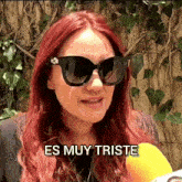 a woman with red hair is wearing sunglasses and says " es muy triste "