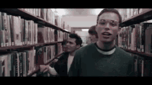 a man wearing goggles is standing in a library surrounded by bookshelves .