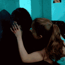 a couple kissing in a dark room with a picture of a woman on the wall behind them