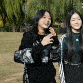 a girl wearing a black adidas sweatshirt stands next to a girl wearing a green adidas sweatshirt