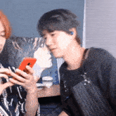 a man and a woman are looking at a red cell phone