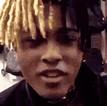 a close up of a man 's face with dreadlocks and a choker around his neck .