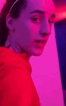 a woman in a red hoodie is standing in a room with purple lights .