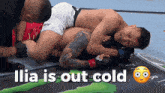 two men are wrestling on a mat and the words ilia is out cold are above them
