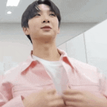 a young man wearing a pink jacket and a white shirt is standing in a room with his hands in the air .