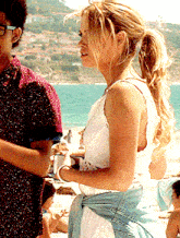 a woman in a white dress is standing next to a man on the beach