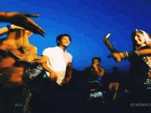 a group of people are dancing in front of a blue sky with the word tanuja on the bottom