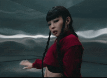 a woman wearing a red sweater and braids looks at the camera