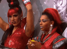 a couple of drag queens are standing next to each other and one is holding a lemon .