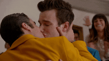 a man in a yellow jacket kisses another man