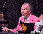 a man in a pink jacket is talking into a microphone in front of a bucket that says kill tony on it
