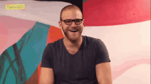 a man wearing glasses is smiling in front of a tailor ed sticker