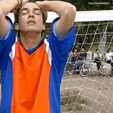 a man in an orange and blue shirt is standing in front of a soccer net