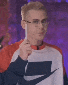 a man wearing glasses and a nike sweatshirt is holding a pen .