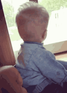 a baby is looking out of a window while sitting in a high chair .