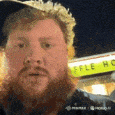 a man with a beard is standing in front of a waffle house sign .
