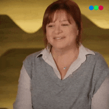 a woman wearing a grey sweater and a white shirt is smiling