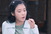 a woman in a light blue jacket is eating a small piece of food