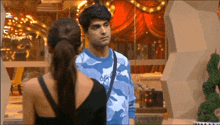 a man and a woman are standing next to each other in a room . the man is wearing a blue camo shirt .