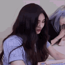 a woman with long dark hair is sitting at a table with a box of candy .