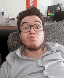 a man with glasses and a beard is sitting on a couch and making a funny face