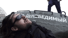 a man wearing sunglasses is laying on top of a tank that says " не победимый " on it