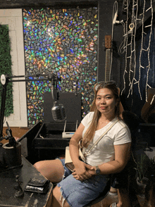a woman sits in front of a microphone in a room with a guitar in the background