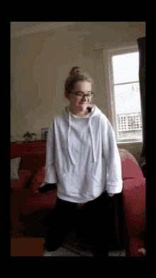 a girl wearing glasses and a white hoodie stands in a living room