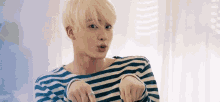 a young man with blonde hair is wearing a striped shirt and a ring on his finger .
