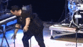 a man is singing into a microphone with a drum set in the background and the website gifrun.com is visible