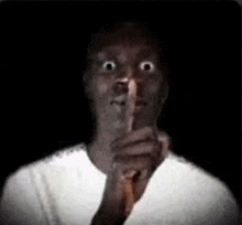 a man in a white shirt is making a shhh gesture with his finger to his mouth .