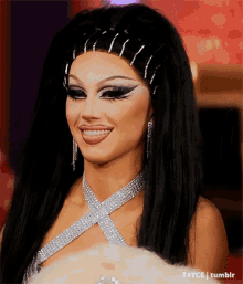 a woman with long black hair is smiling and wearing a silver dress and necklace .